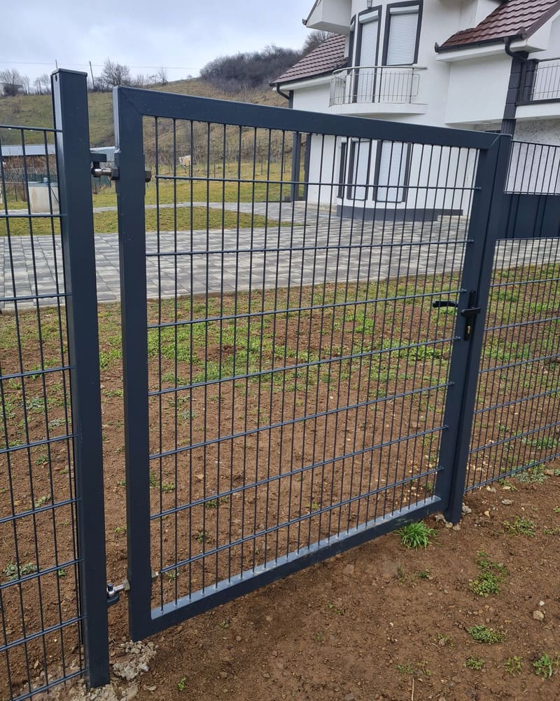 Derë oborri me një kanat nga paneli 2D, me dorëz dhe bravë, para një shtëpie të bardhë